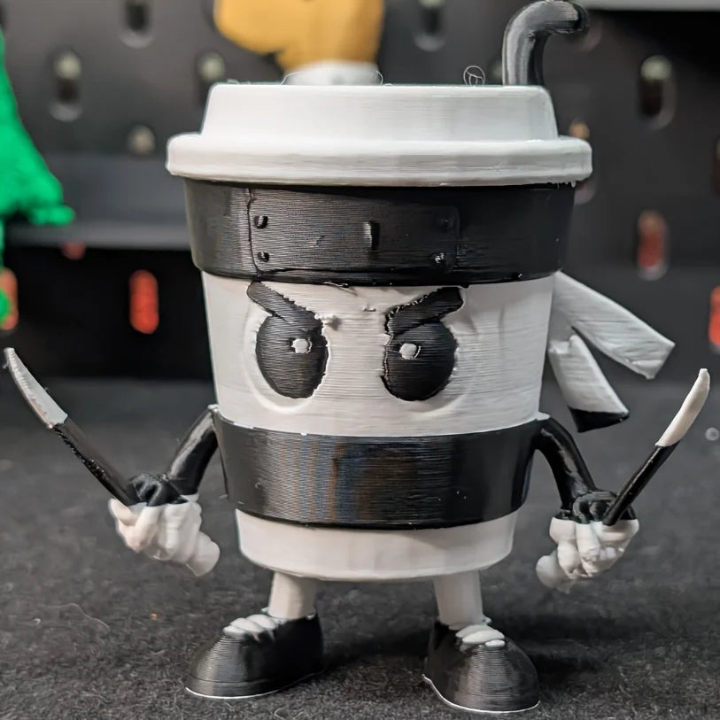 3D-printed Cappuccini Assassini Collector's Edition -  Animated character made from a coffee cup on a wooden surface with background kitchen items